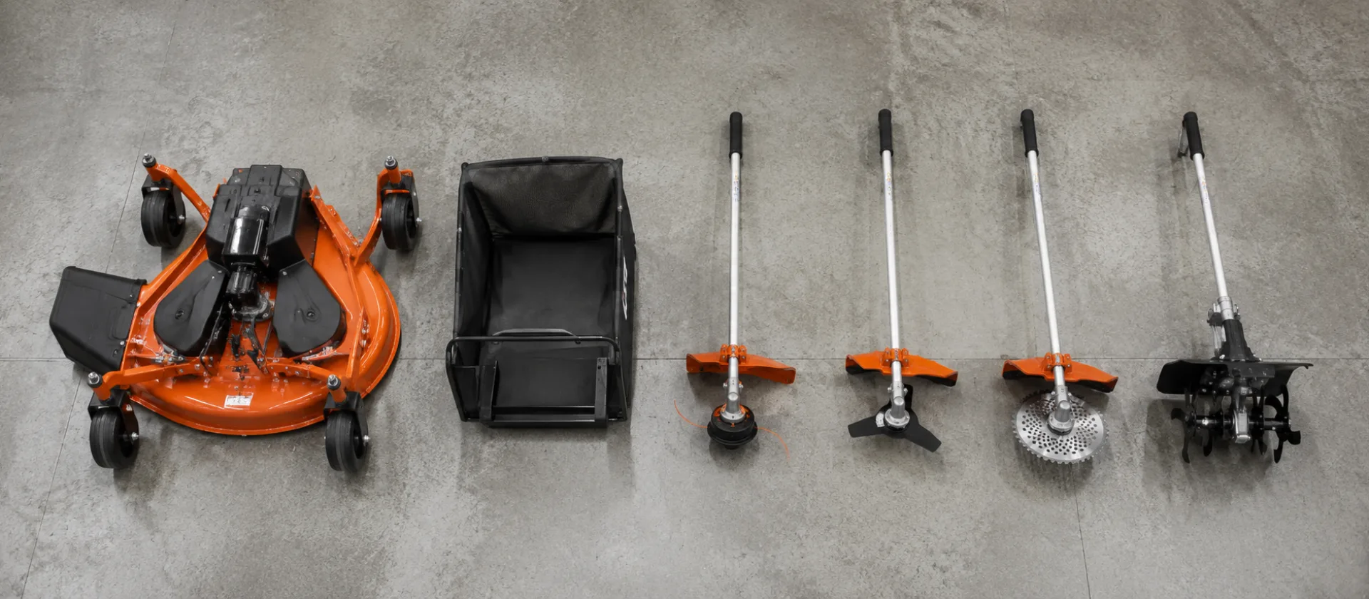 A ride-on mower deck, a grass catcher and four Combi attachment heads laid out on a workshop floor, seen from above